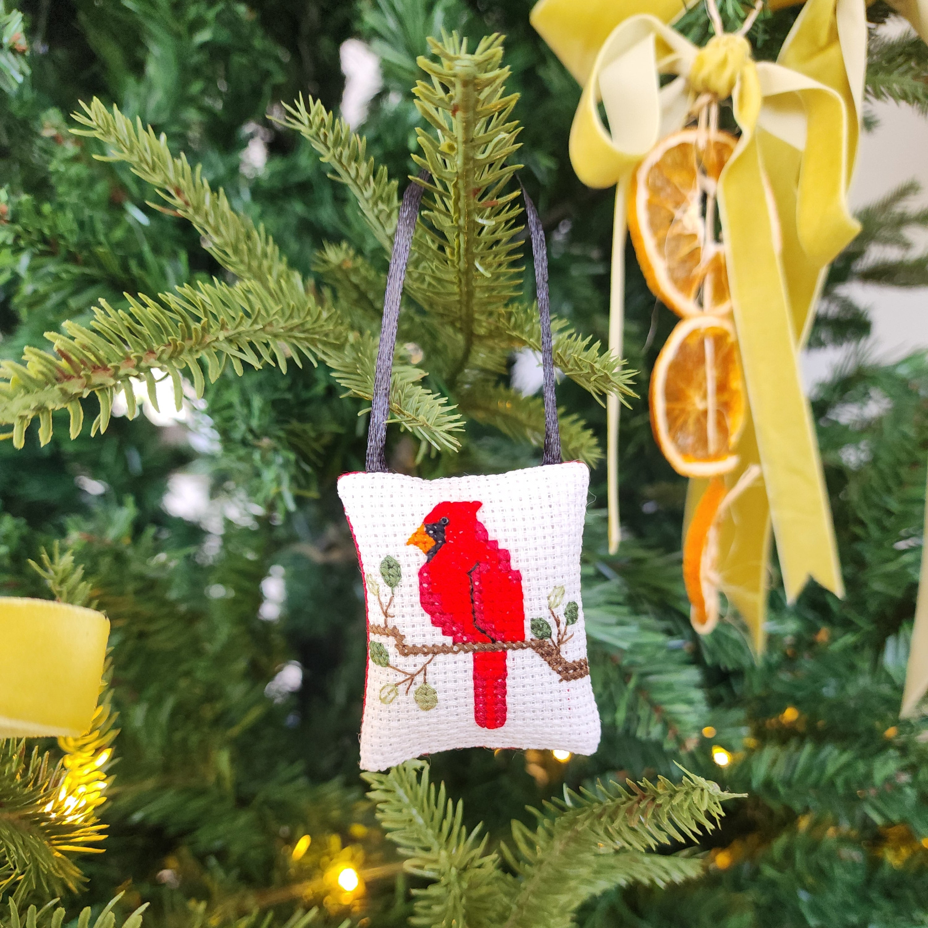Decorative red cardinal bird ornament on a Christmas tree with green branches and lights.