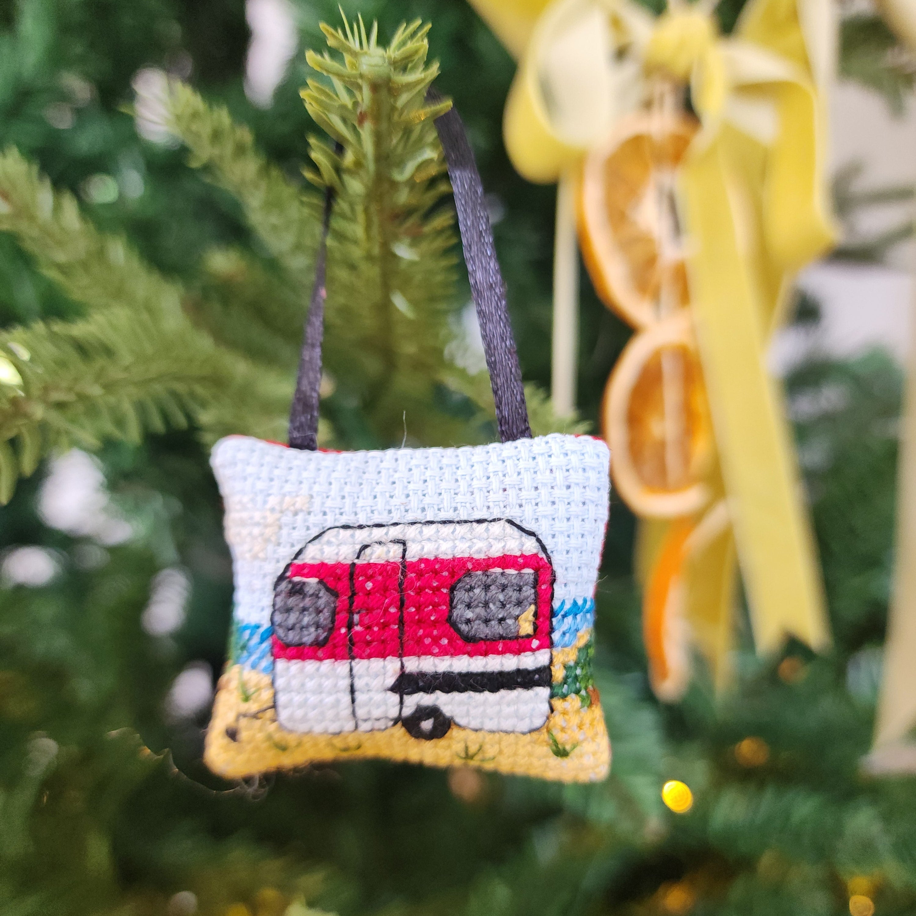 Decorative ornament shaped like a camper van hanging on a Christmas tree.