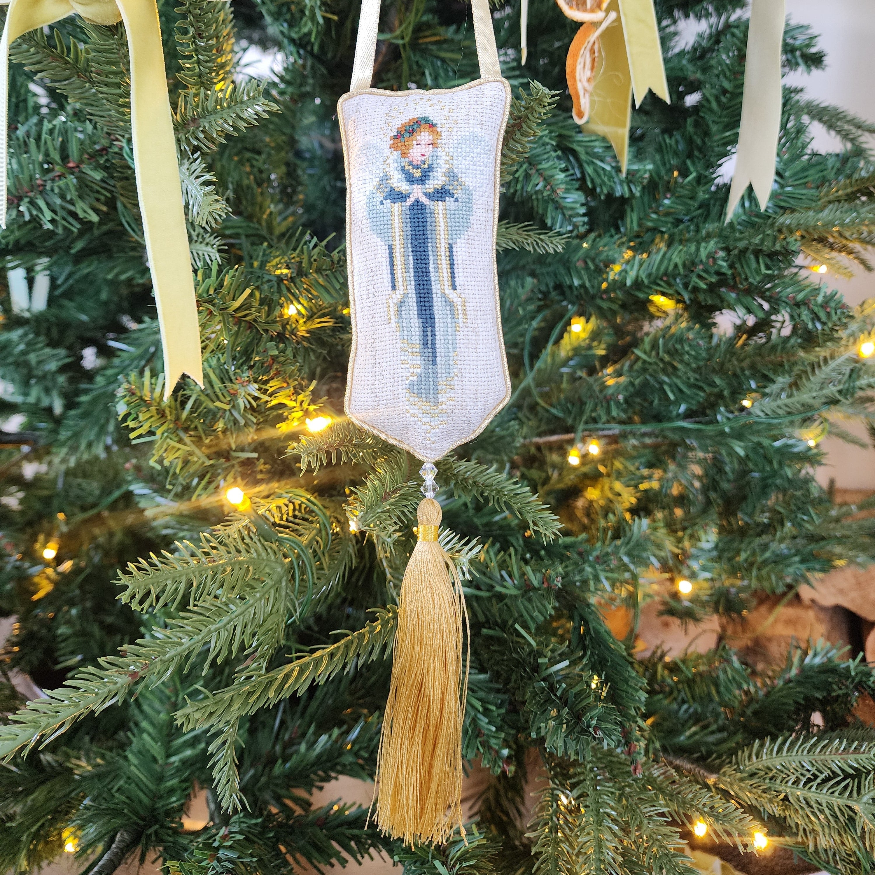 Decorative angel ornament with a tassel hanging on a Christmas tree.