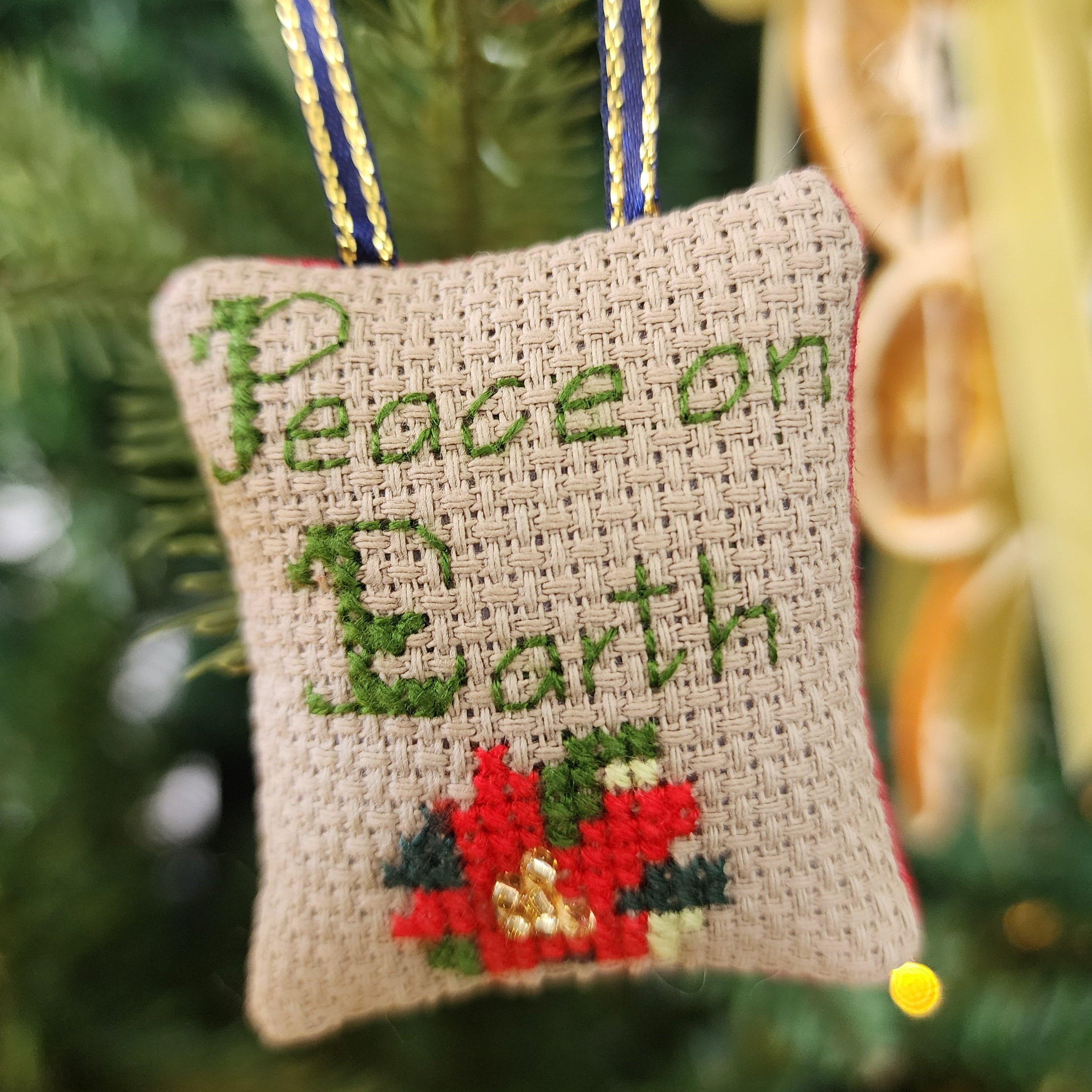 Decorative Christmas ornament with 'Peace on Earth' text and poinsettia design on a tree.